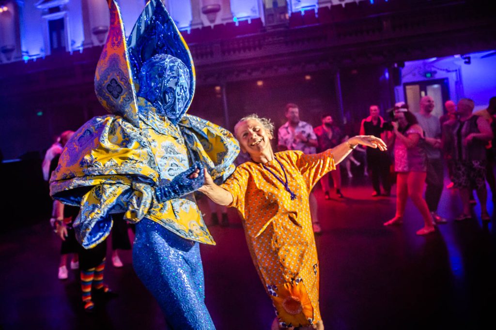 The Coming Back Out Salon, Sydney WorldPride 2023 by All The Queens Men. Image: Bryony Jackson. Description: The Huxleys, dressed in royal blue and yellow dance with an older person at the Sydney Town Hall.