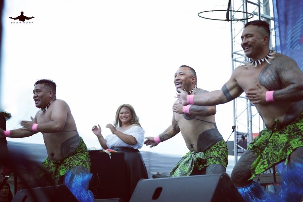 An image of four traditional samoan dancers on stage and a DJ smiling and clapping along.